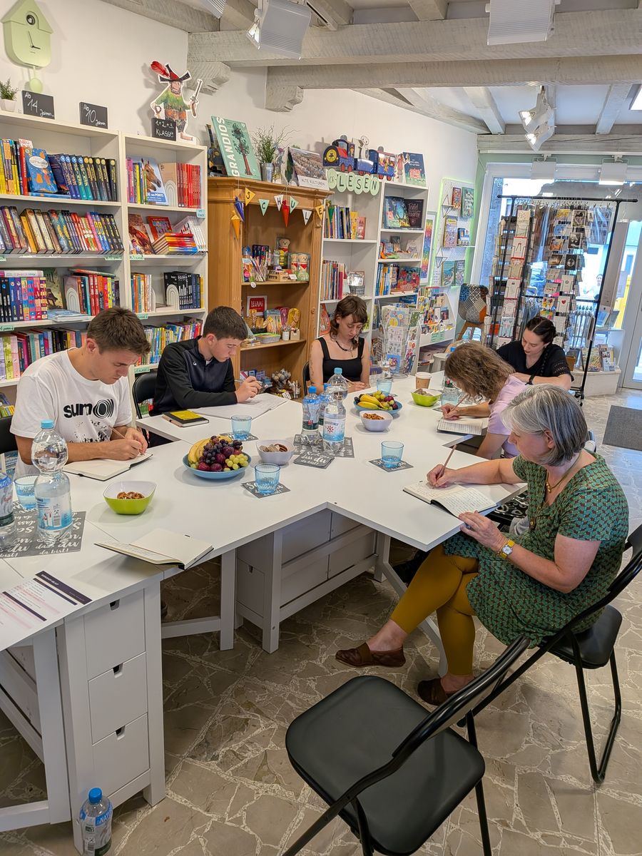 Teilnehmende schreiben konzentriert an einem langen Tisch zwischen Bücherregalen im Buchladen Kopfkino